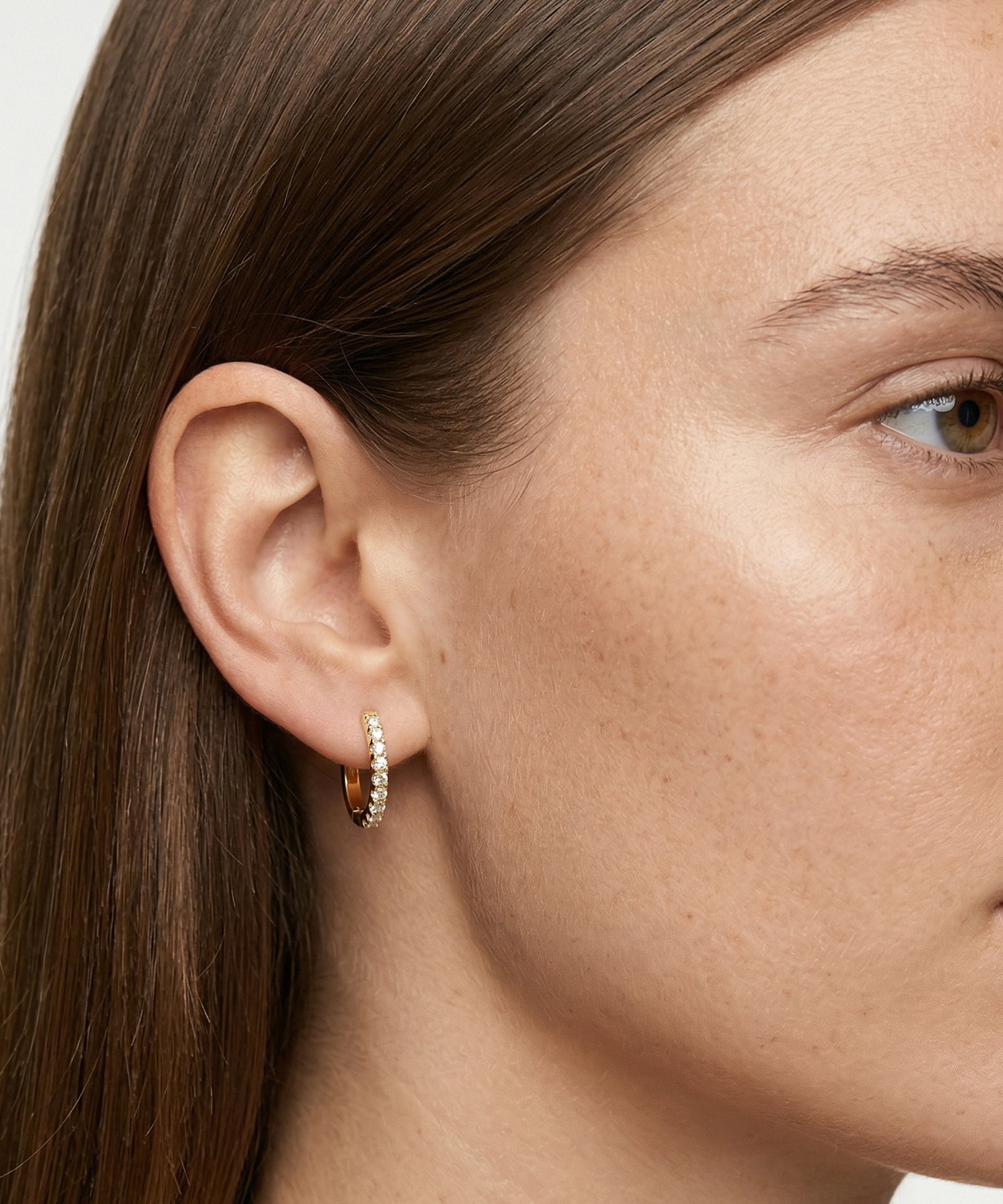 Close-up of a person wearing a silver hoop earring with small stones.
