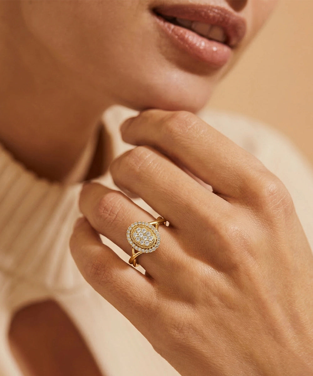 Close-up of a hand wearing a gold ring with a diamond design against a neutral background