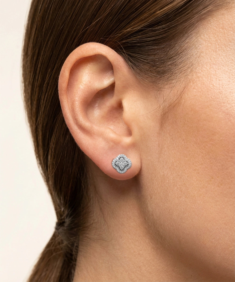 Close-up of an ear wearing a silver earring with a clear gemstone on a neutral background