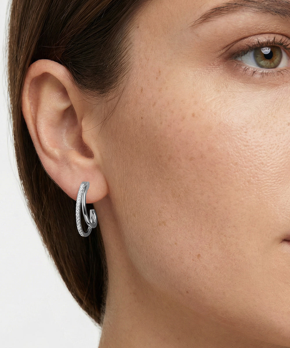 Close-up of a woman's ear wearing a silver hoop earring on a white background