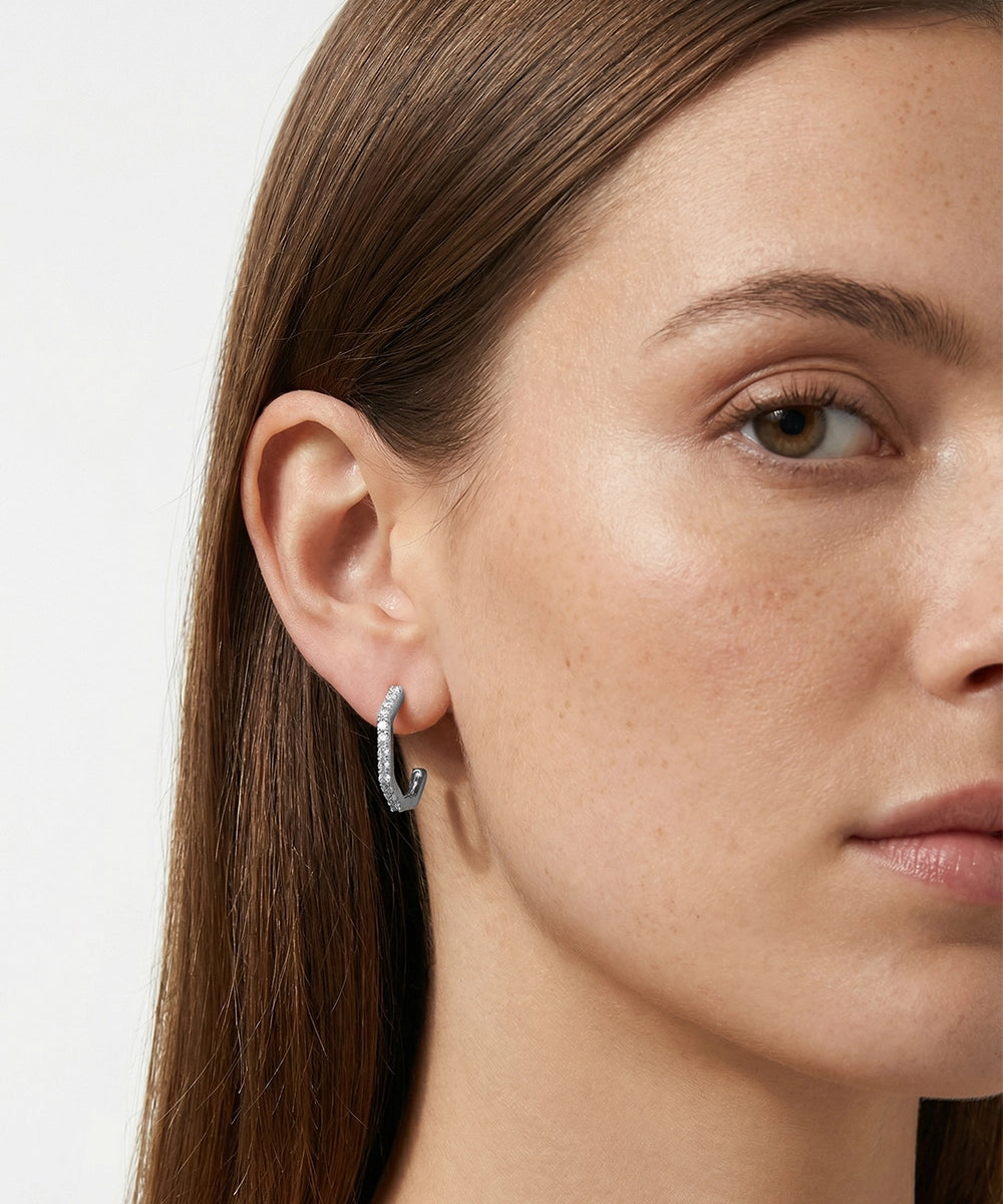 Close-up of a woman wearing a silver hoop earring on a plain background