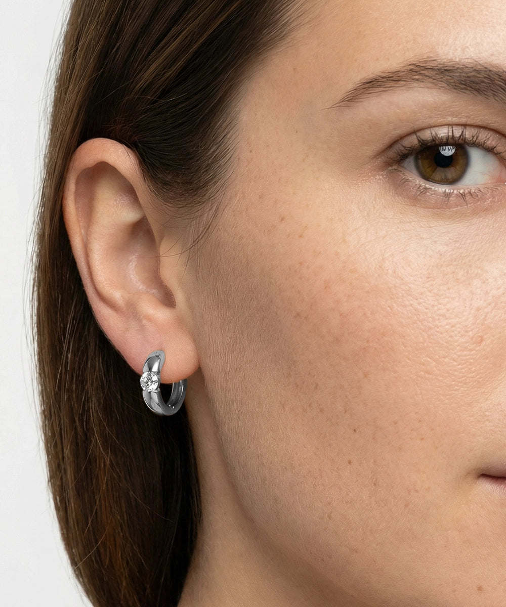 Close-up of a woman wearing a silver earring with a clear gemstone.