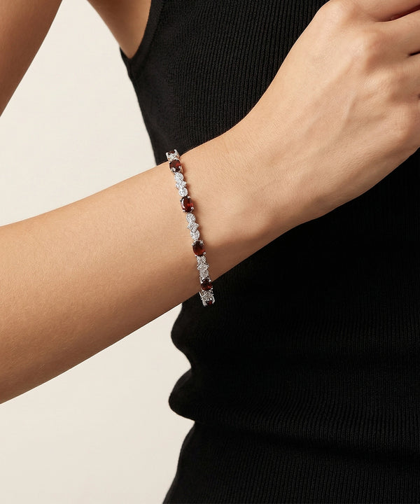 Bracelet with red and clear stones on a person's wrist against a neutral background
