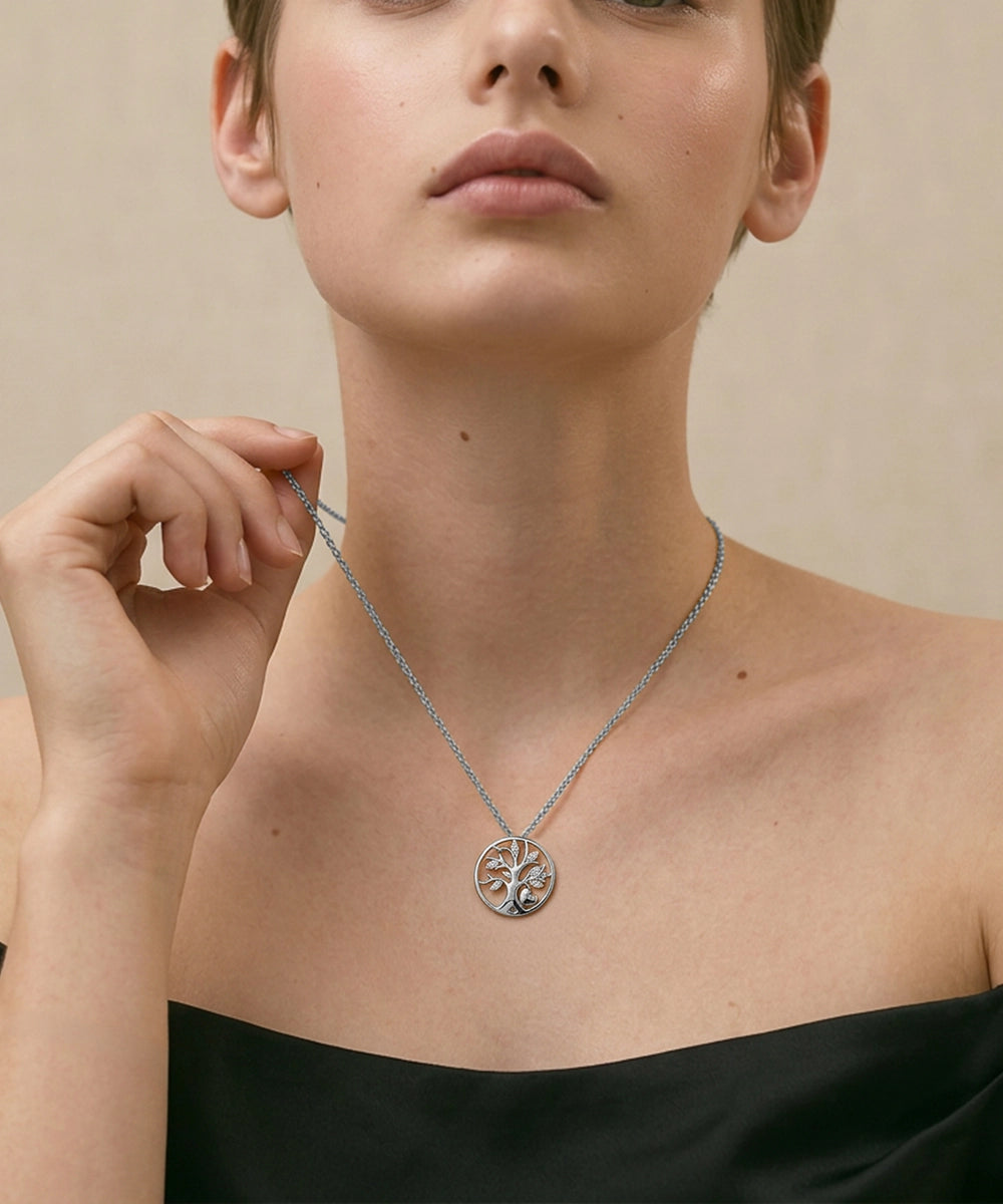 Person wearing a silver necklace with a tree of life pendant against a beige background