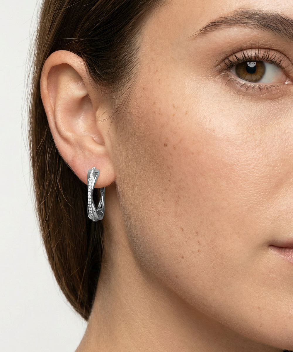 Close-up of a woman wearing silver hoop earrings with a neutral background