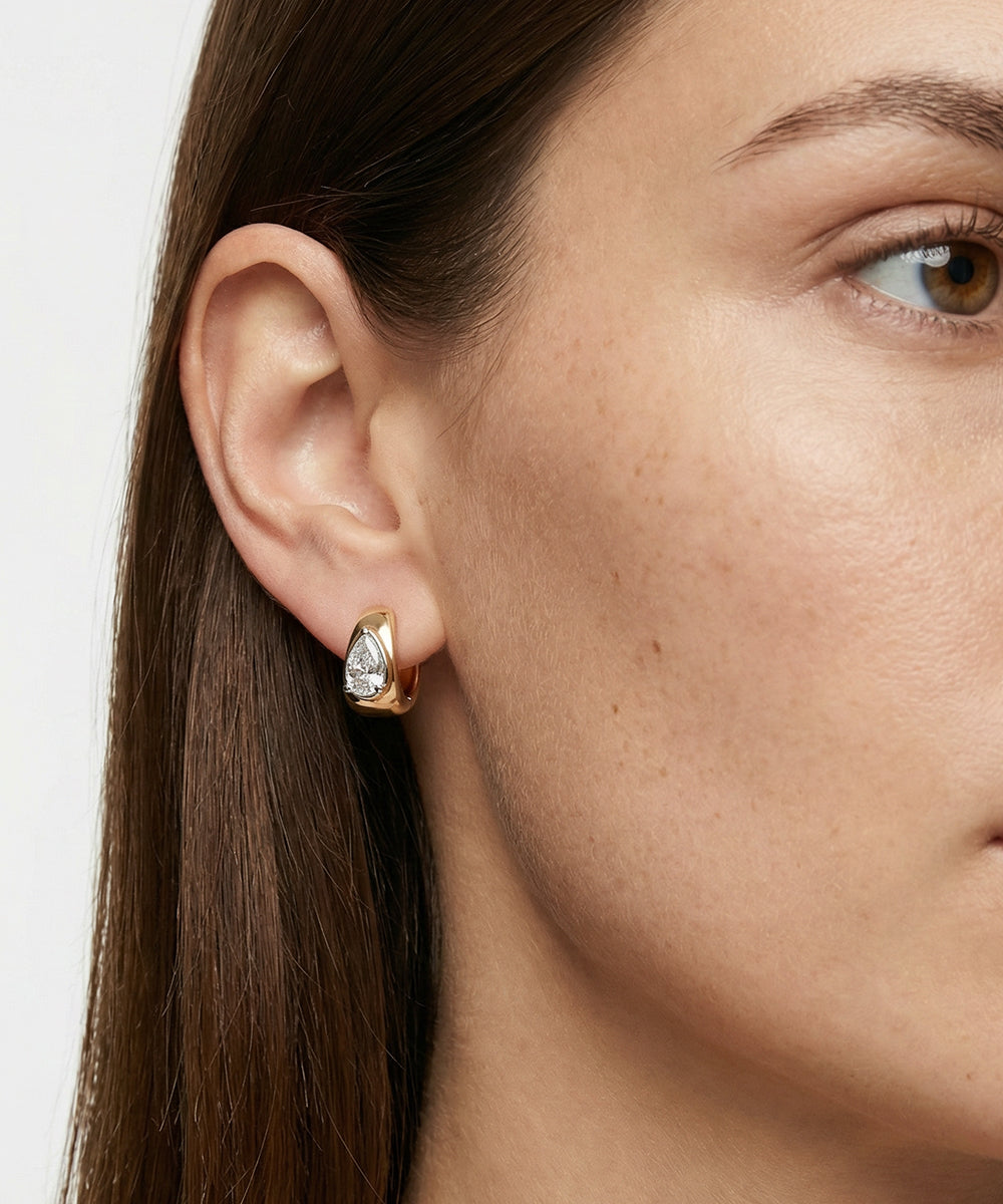 Close-up of a woman wearing a gold earring with a clear gemstone.
