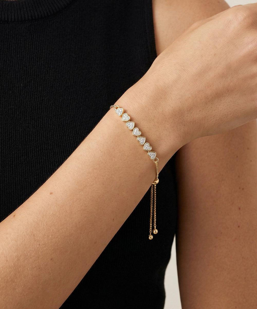 Gold bracelet with heart-shaped beads on a person's wrist against a black background
