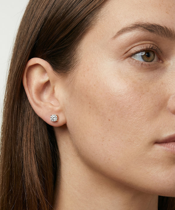 Close-up of a woman wearing diamond stud earrings with a neutral background