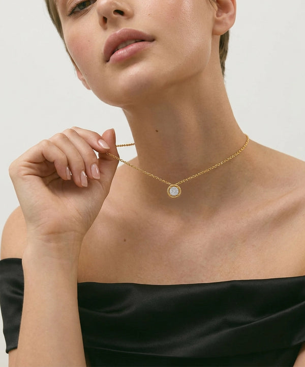 Woman wearing a silver necklace with a circular pendant on a plain background