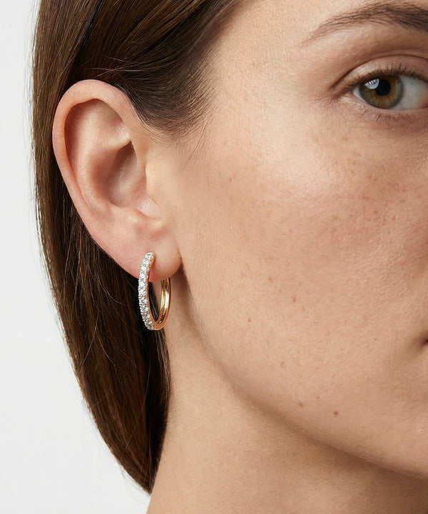Close-up of a person wearing gold hoop earrings with clear stones.