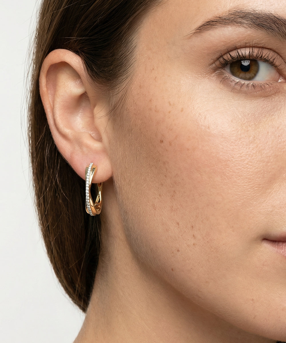 Close-up of a woman wearing gold hoop earrings with a neutral background