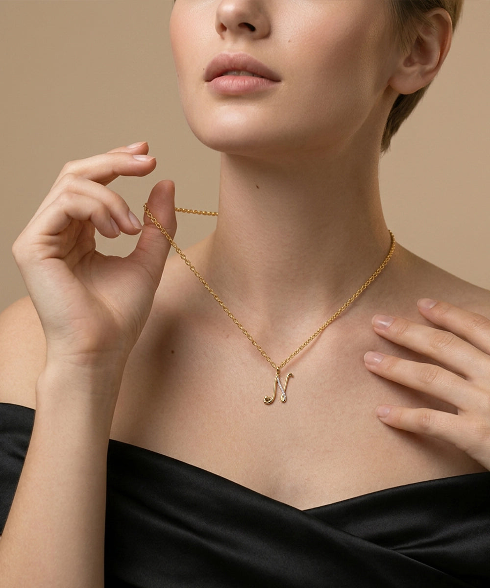 Woman wearing a gold necklace with a 'N' pendant against a neutral background