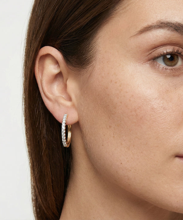 Close-up of a person wearing gold hoop earrings with a neutral background