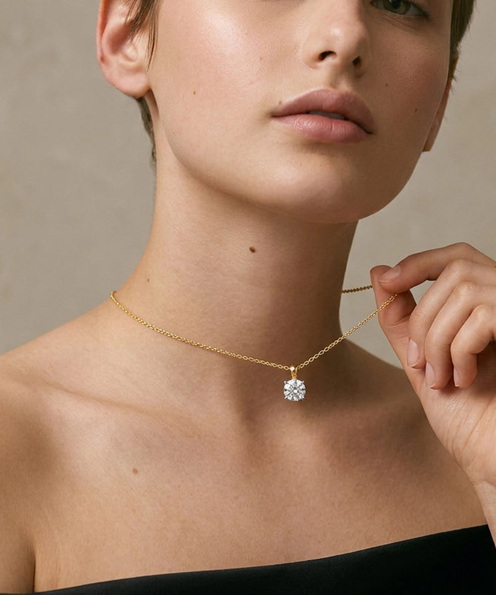 Woman wearing a gold necklace with a diamond pendant against a neutral background