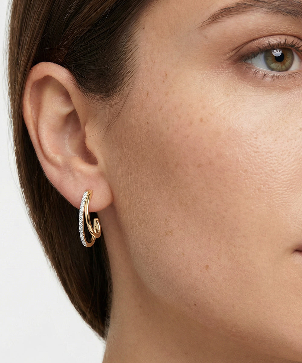 Close-up of a person wearing gold hoop earrings with a neutral background