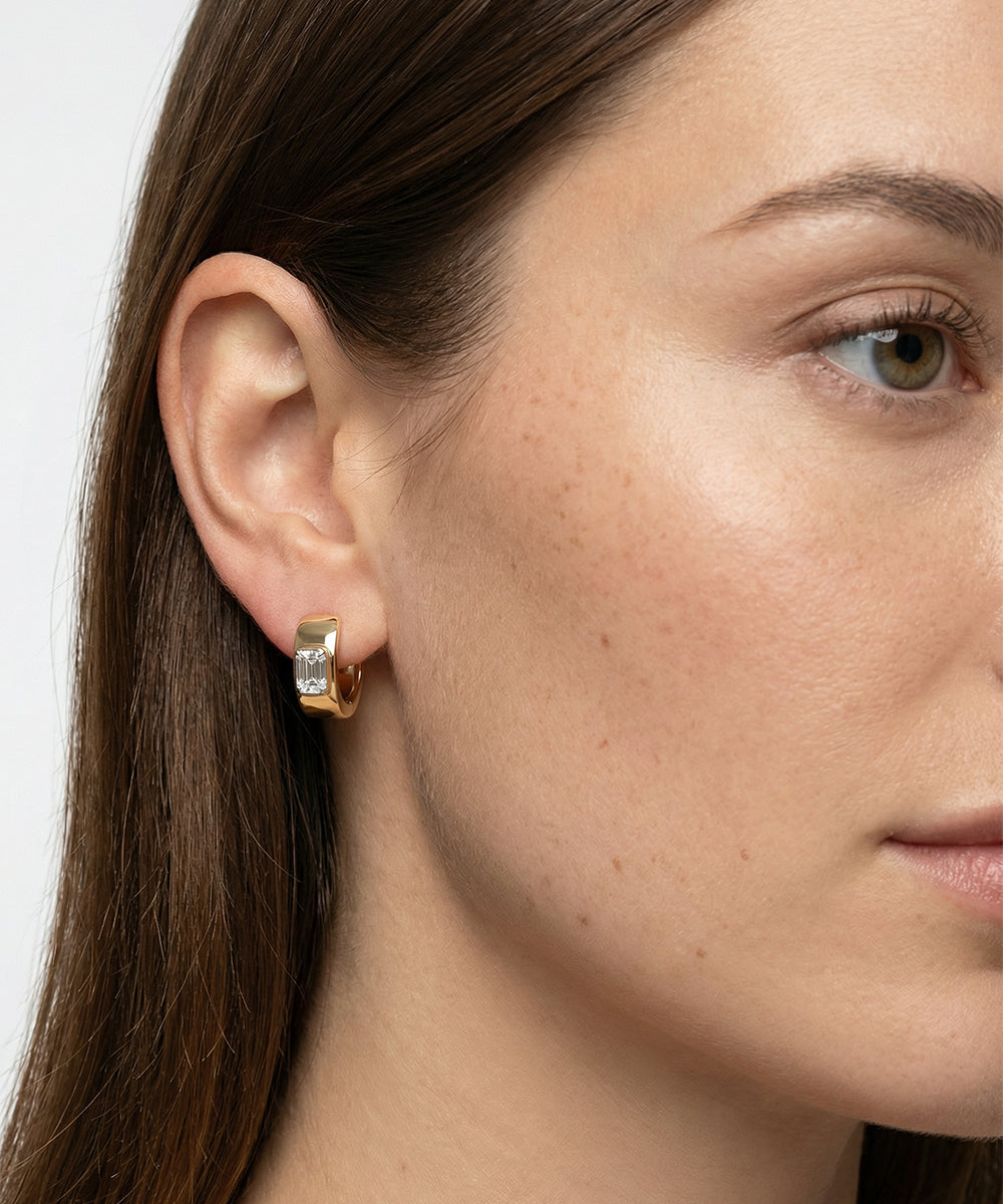 Close-up of a woman wearing gold hoop earrings with a clear gemstone on a white background