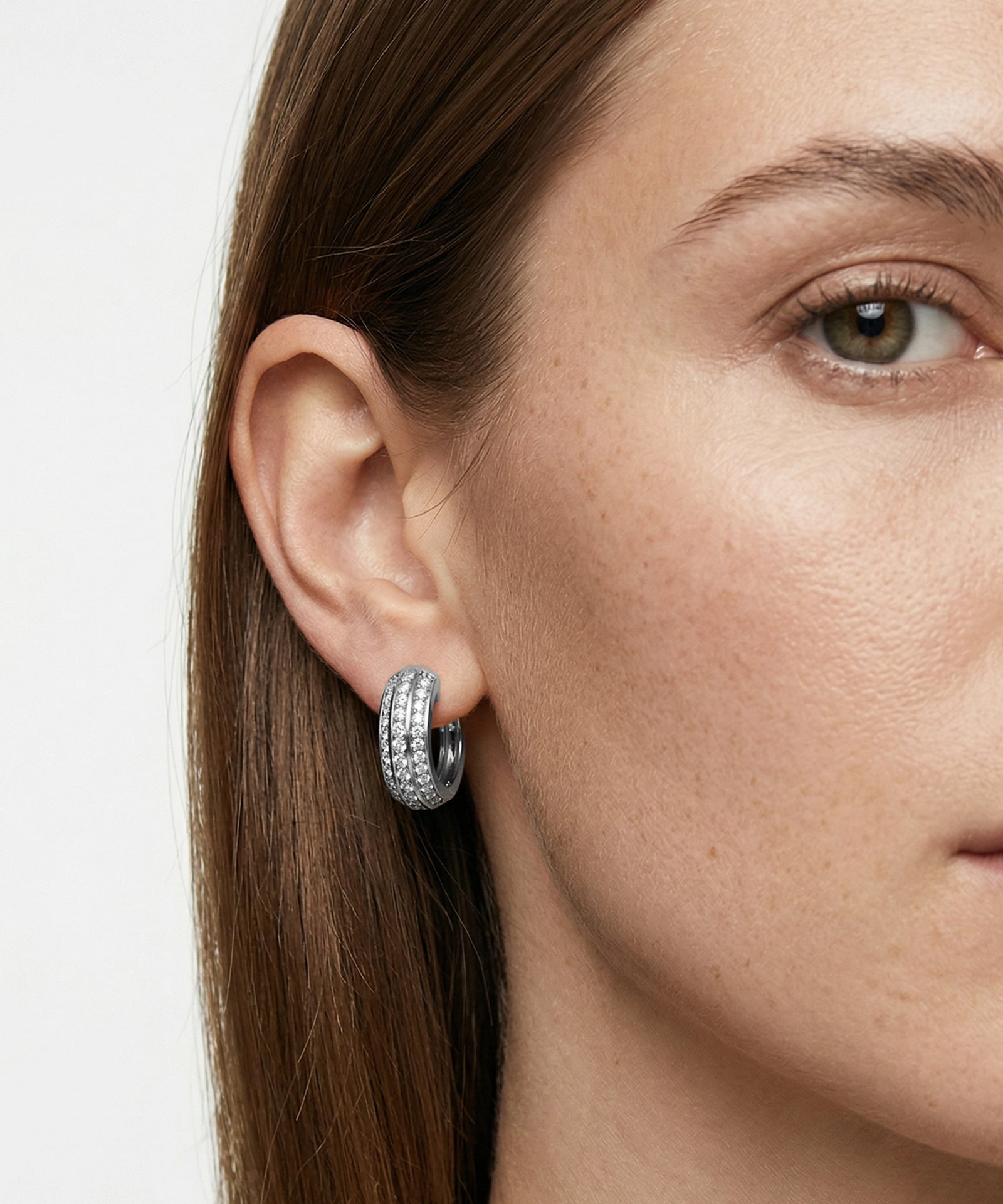 Close-up of a woman wearing silver hoop earrings with a plain background
