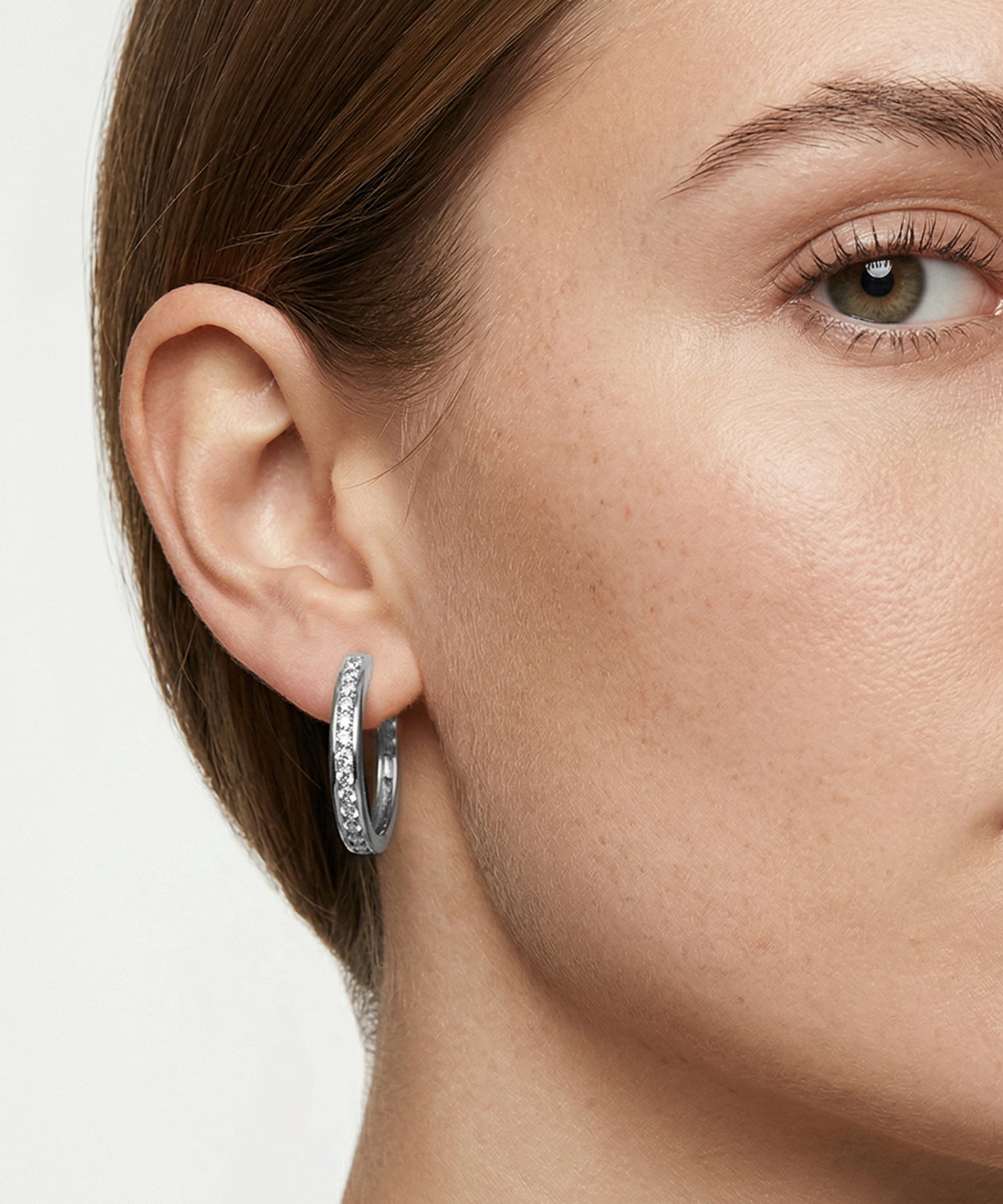 Close-up of a woman's ear wearing a silver hoop earring with a blurred background