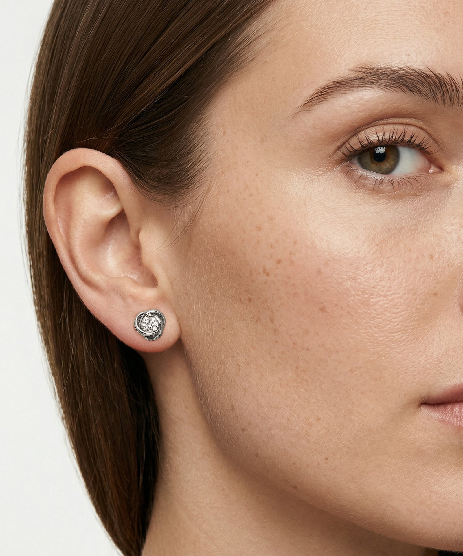 Close-up of a woman wearing a silver earring with a clear gemstone.