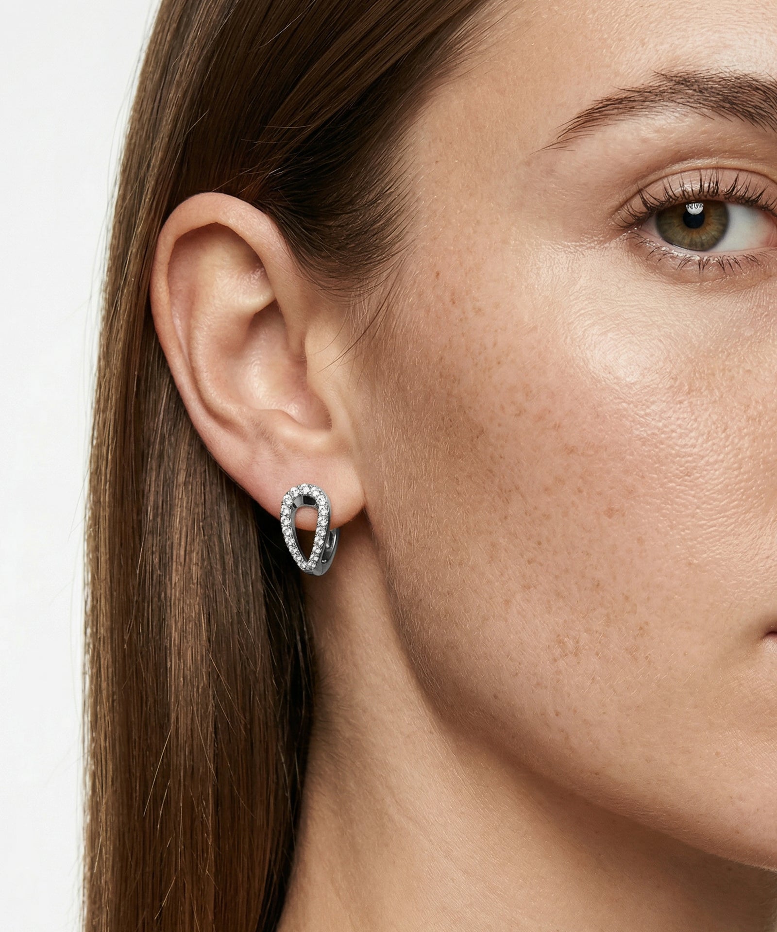 Close-up of a woman wearing a silver hoop earring with a white background
