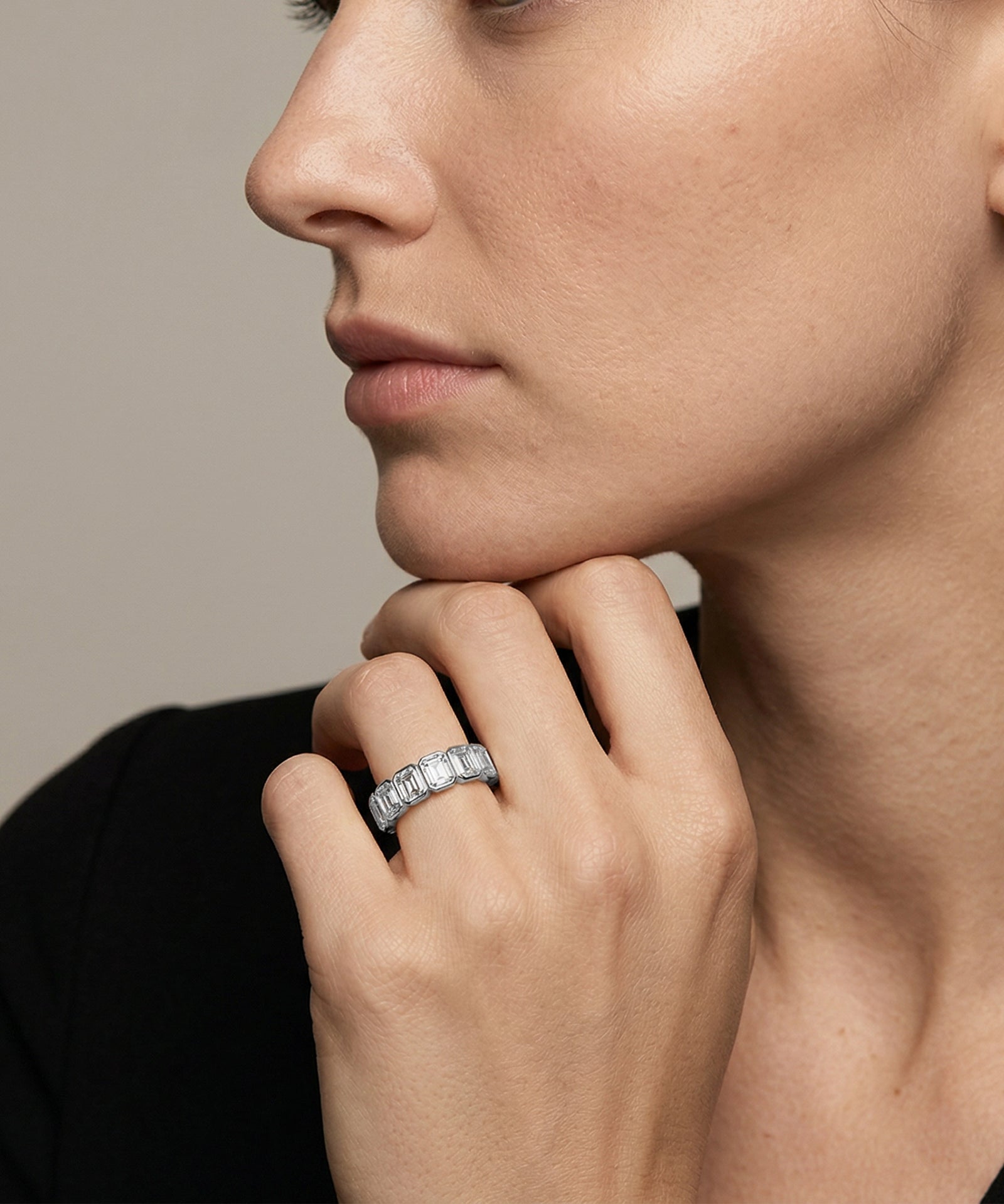Close-up of a woman's hand wearing a diamond ring with a neutral background