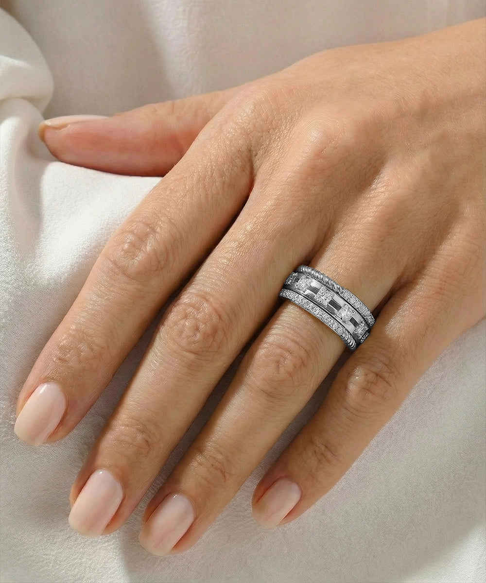 Hand wearing a silver ring with intricate design on a light background