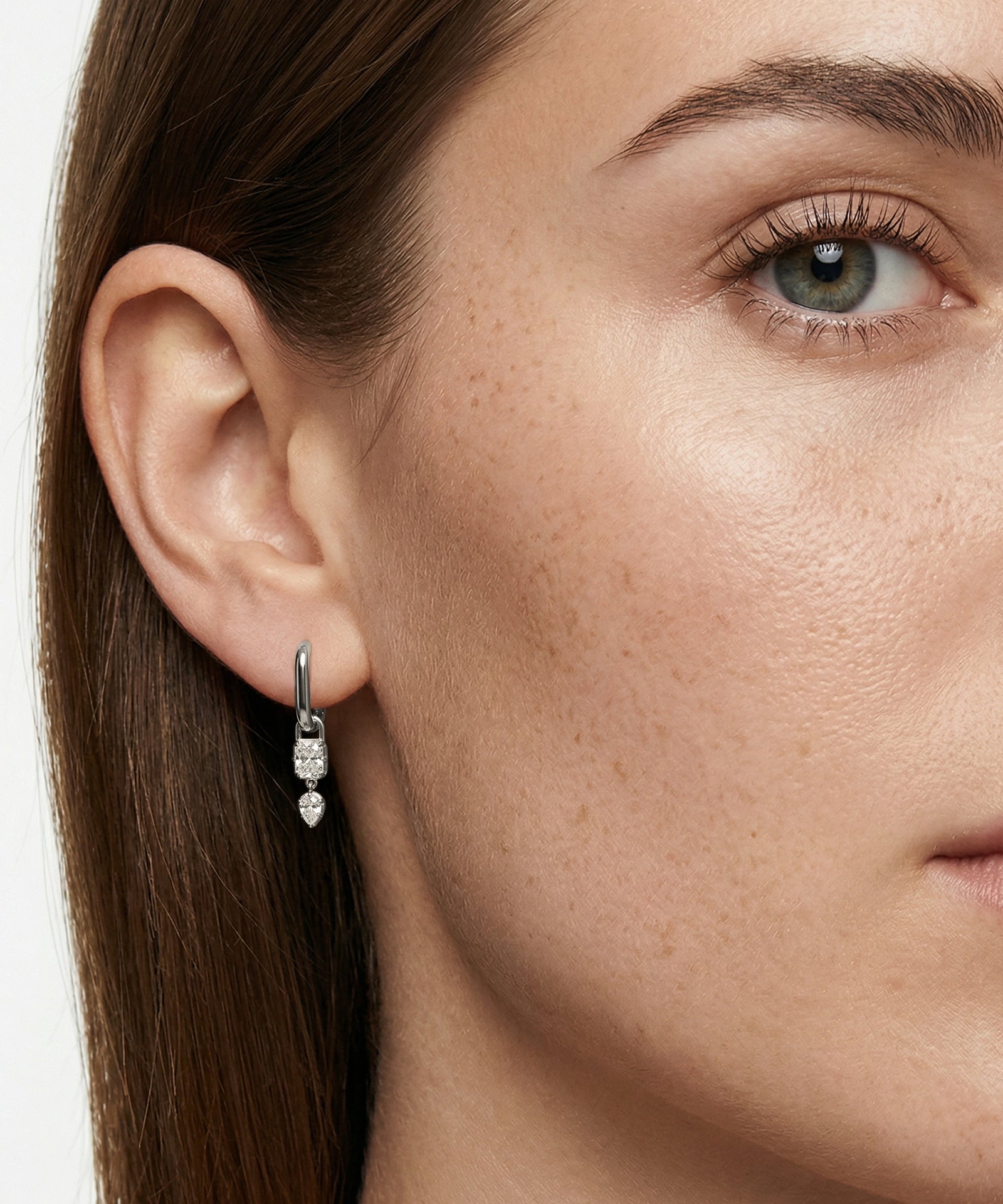 Close-up of a woman's ear wearing a diamond earring with a neutral background