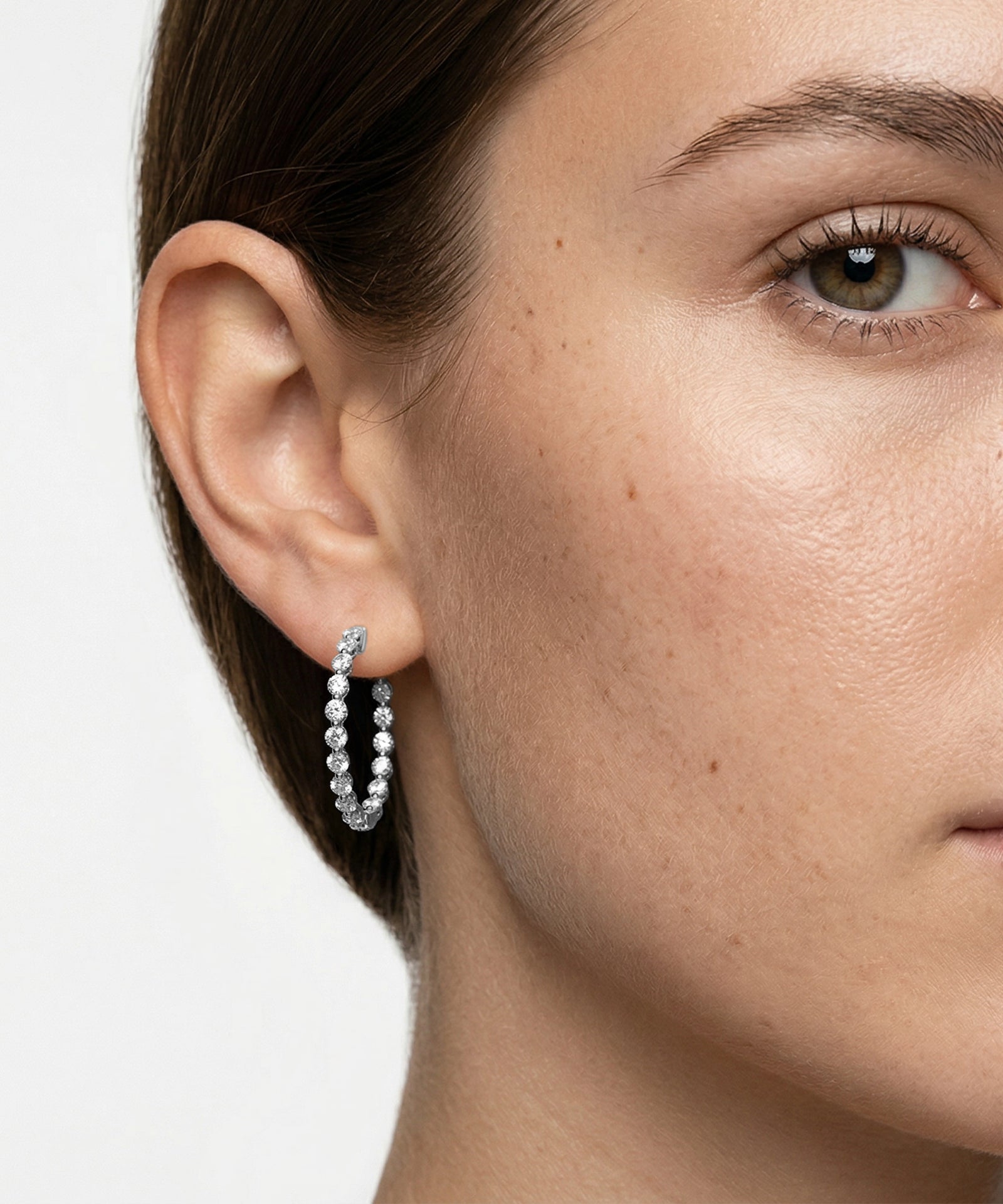 Close-up of a person wearing gold hoop earrings with pearls on a neutral background