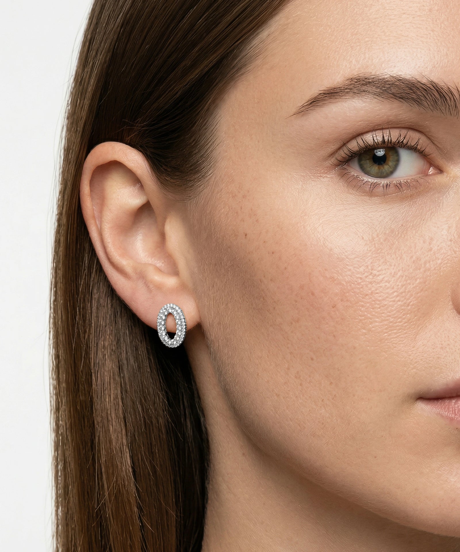 Close-up of a woman wearing a silver hoop earring with a plain background