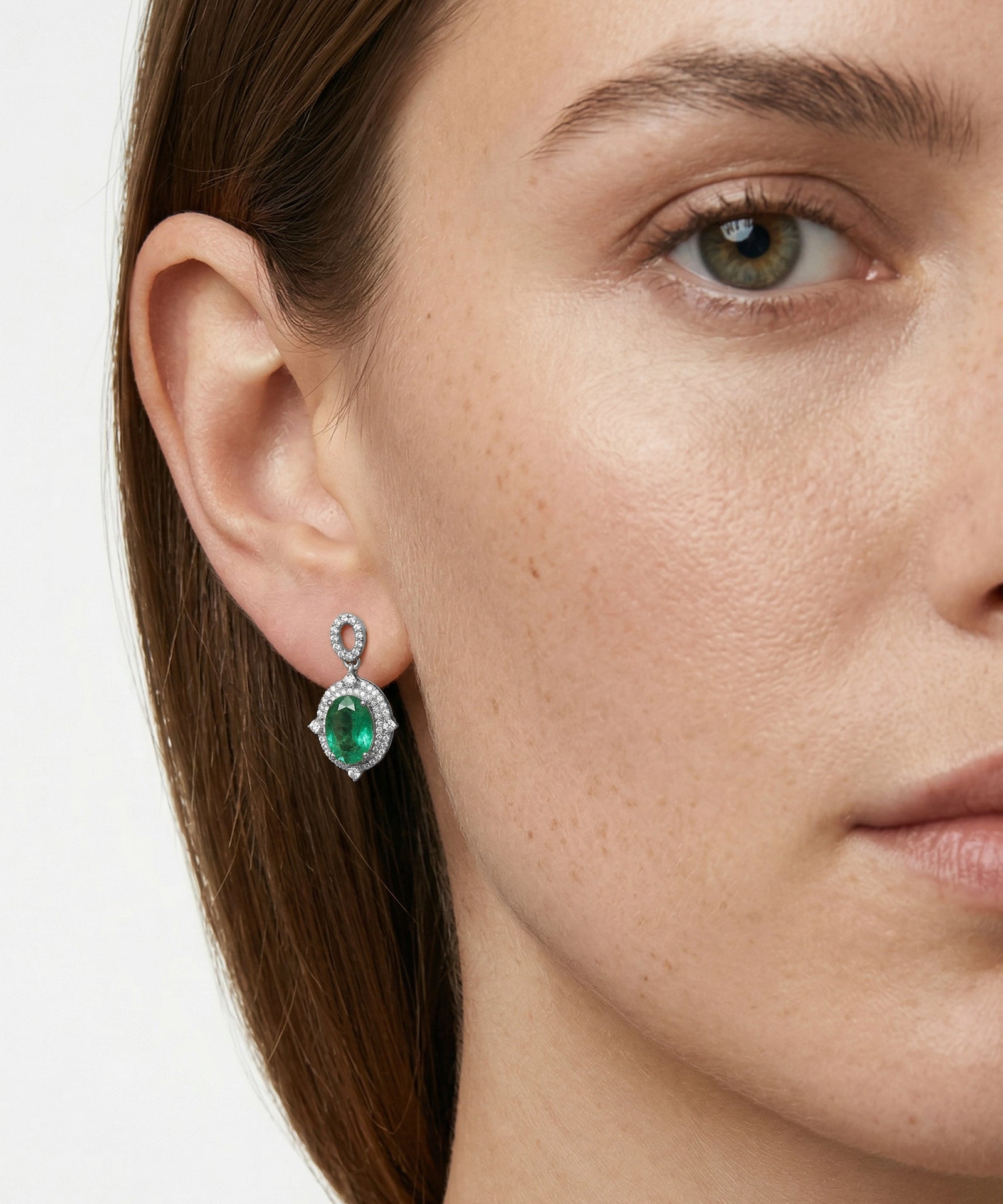 Close-up of a woman wearing emerald green earrings with a white background