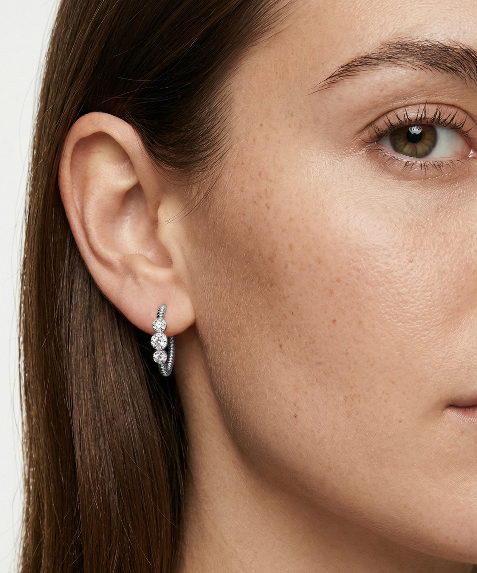 Close-up of a woman wearing a diamond earring with a neutral background
