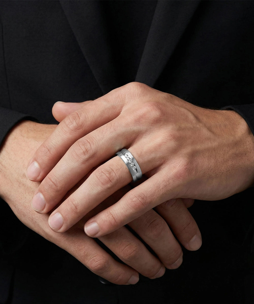 Man wearing a wide white gold or platinum men's wedding band with a matte satin finish, featuring a central grooved channel set with round diamonds, styled on a hand.