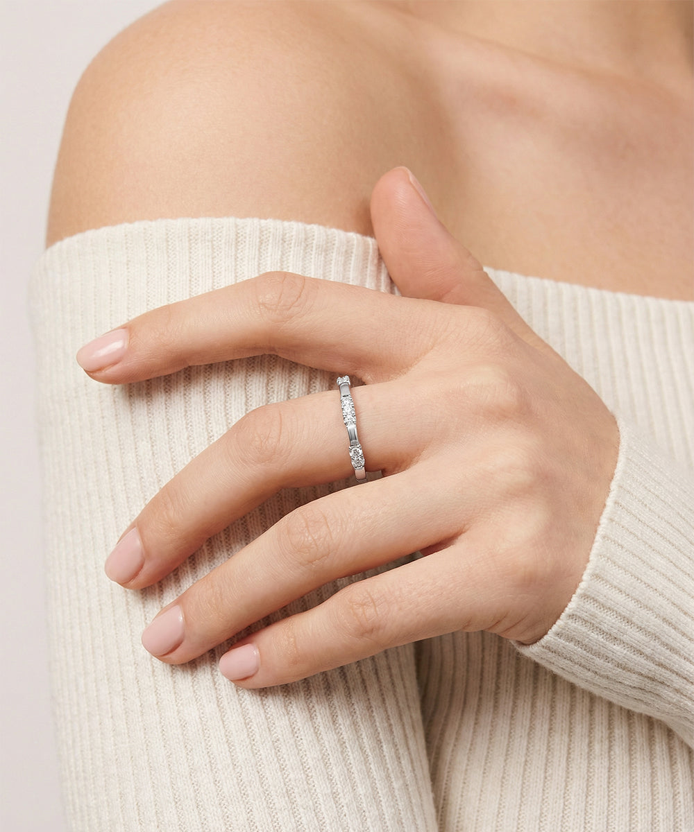 Hand wearing a silver ring with a beige sweater on a light background