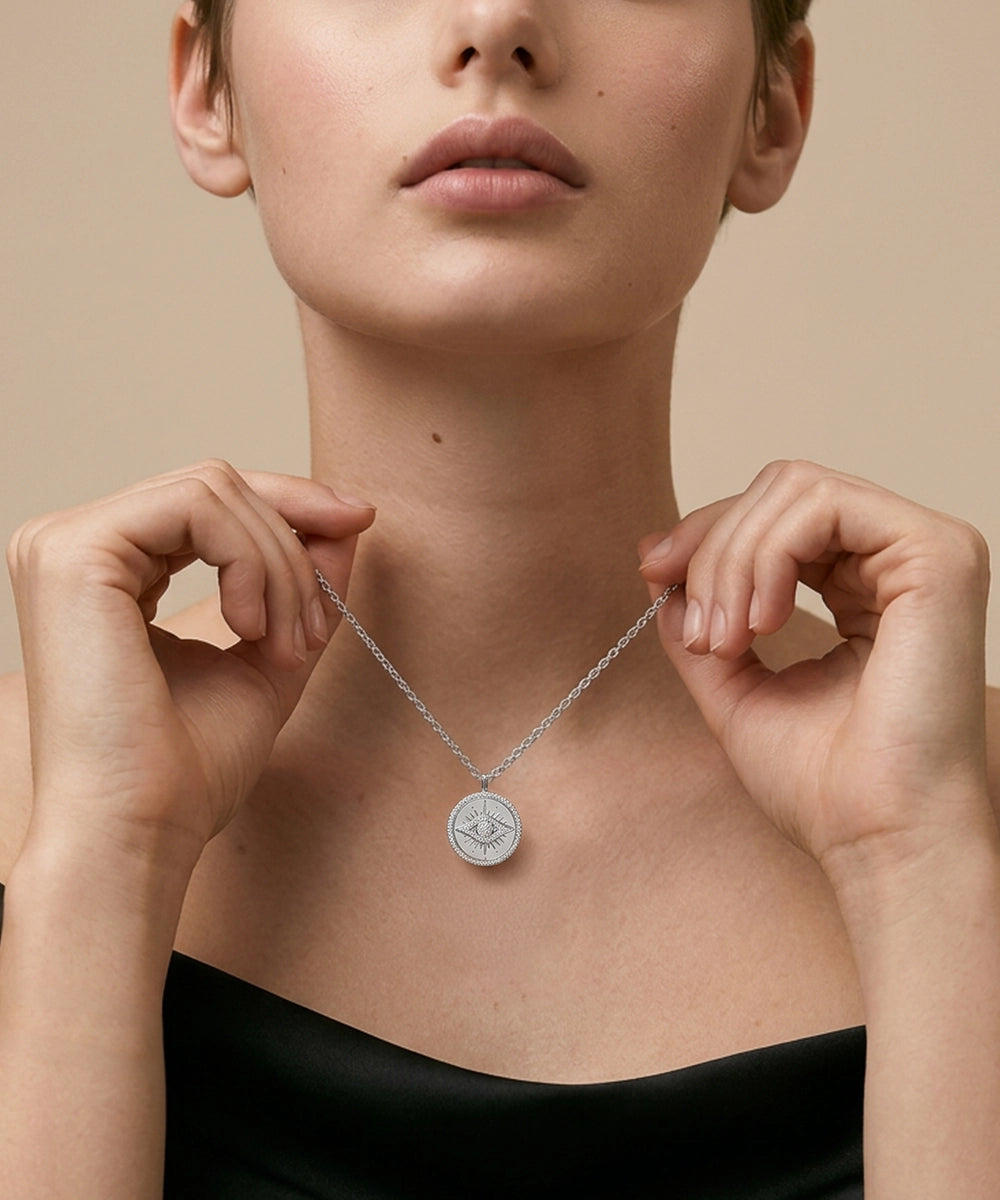 Person wearing a silver necklace with a pendant against a neutral background