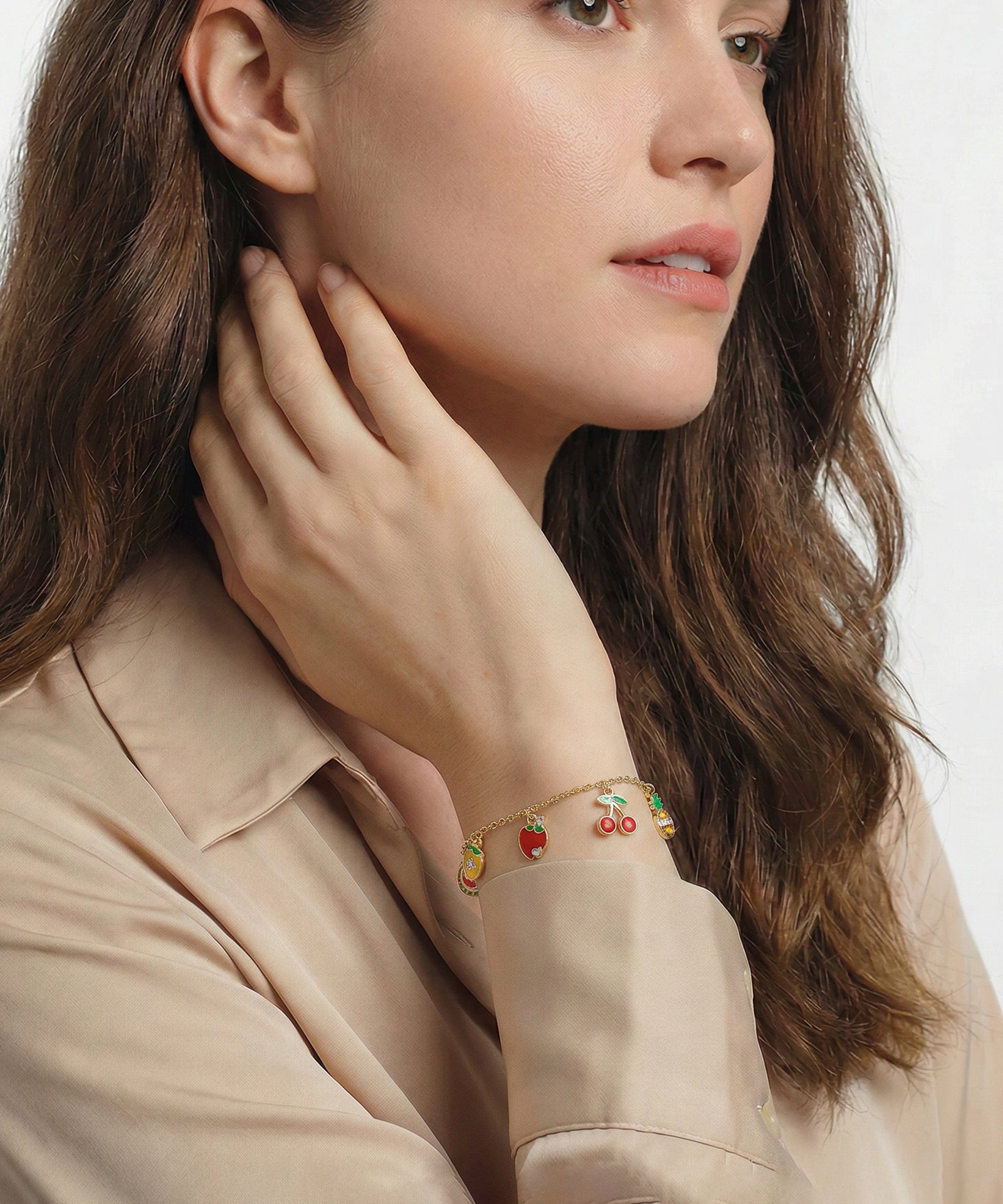 Woman wearing a bracelet with fruit charms on a plain background
