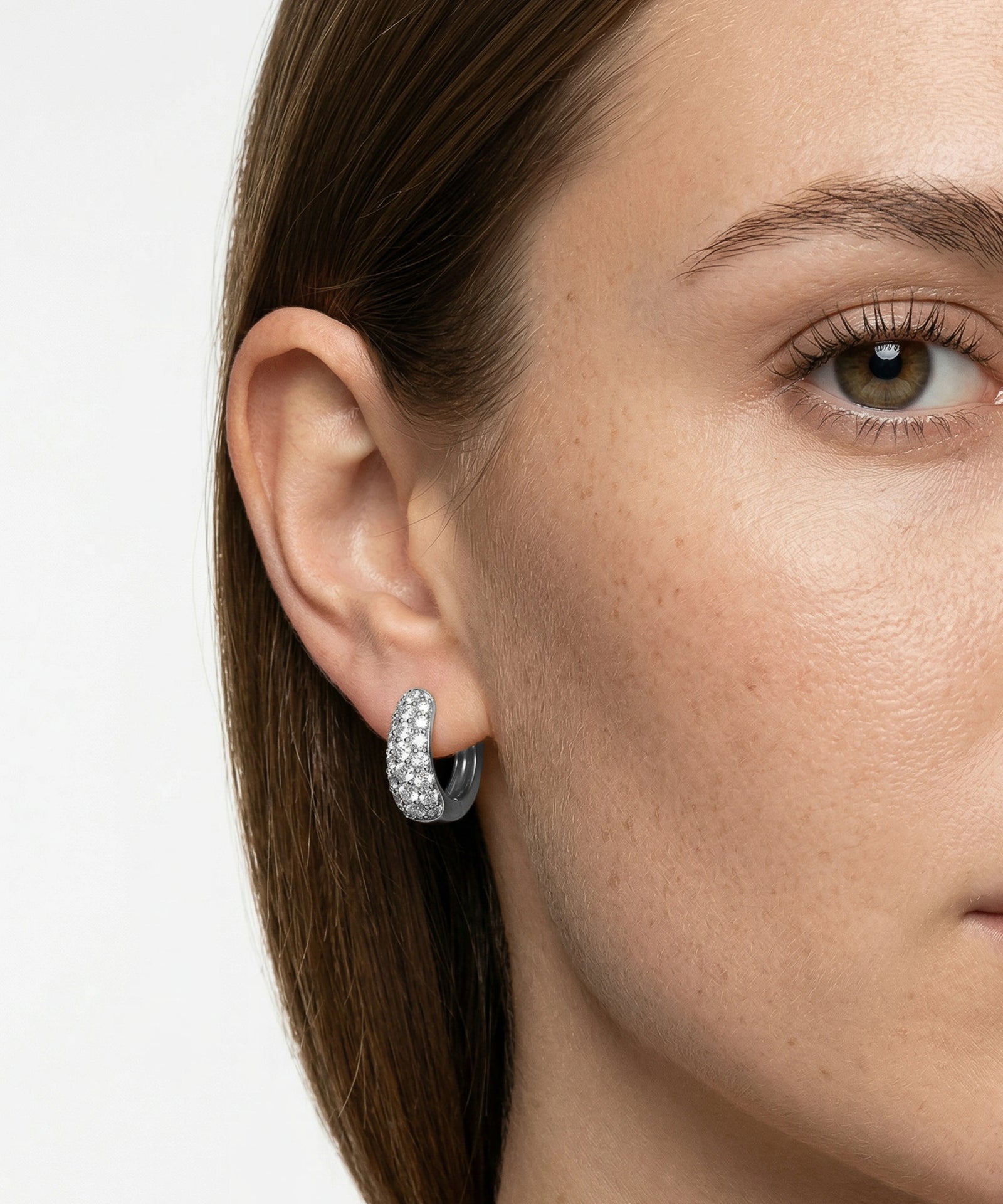 Close-up of a woman wearing a silver hoop earring with clear stones on a white background