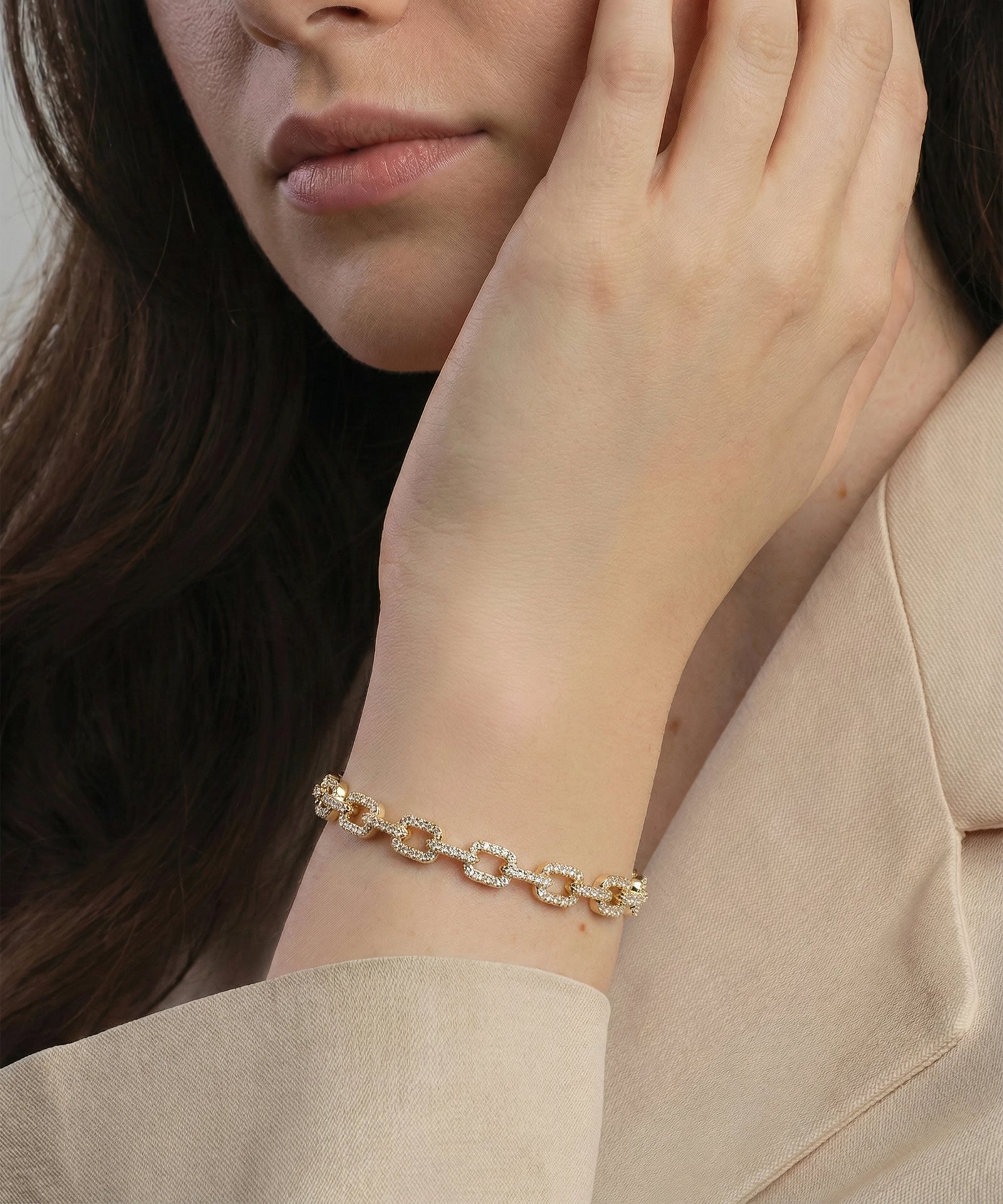 Close-up of a person wearing a gold bracelet on a neutral background