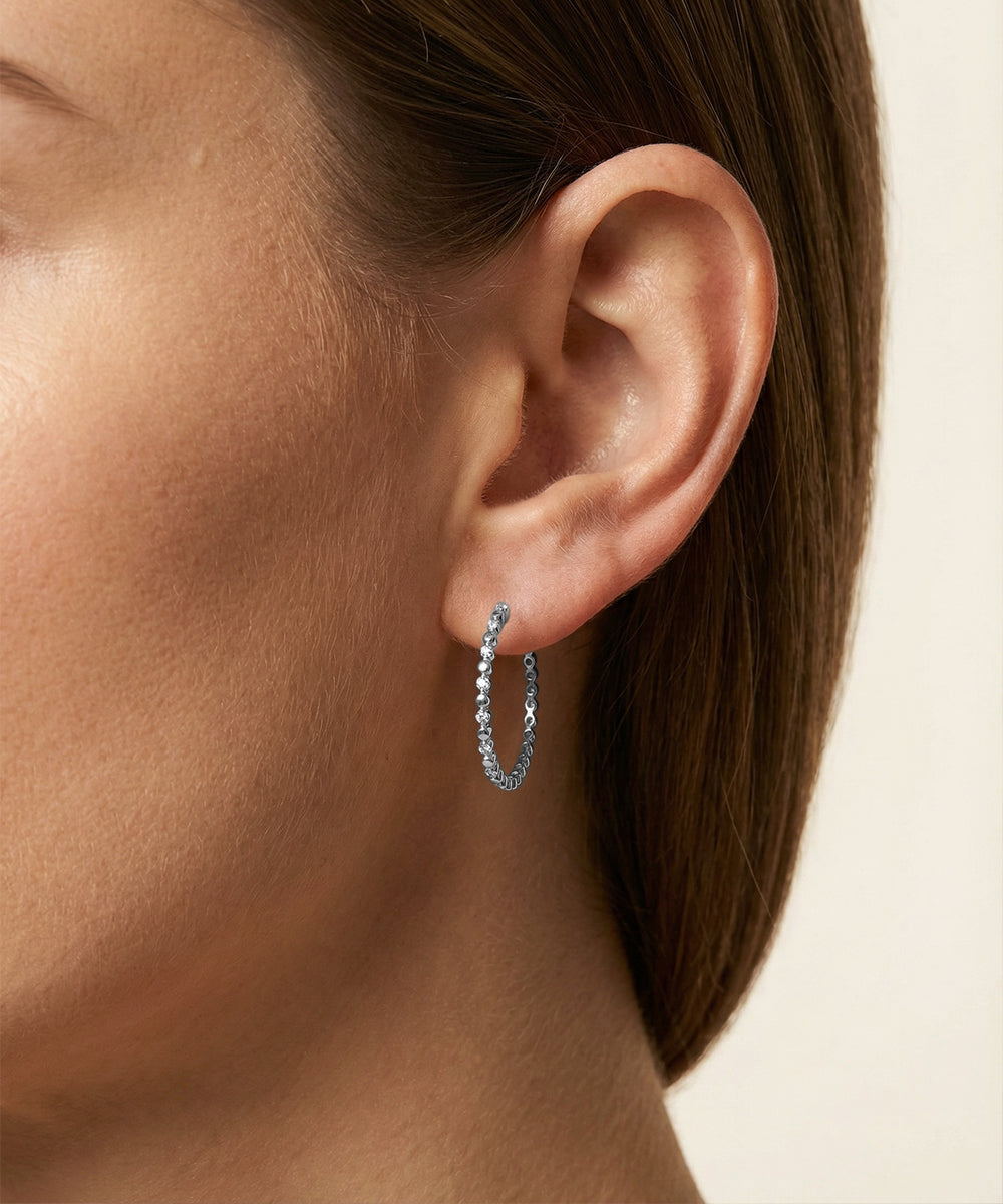 Close-up of an ear wearing a silver hoop earring on a neutral background