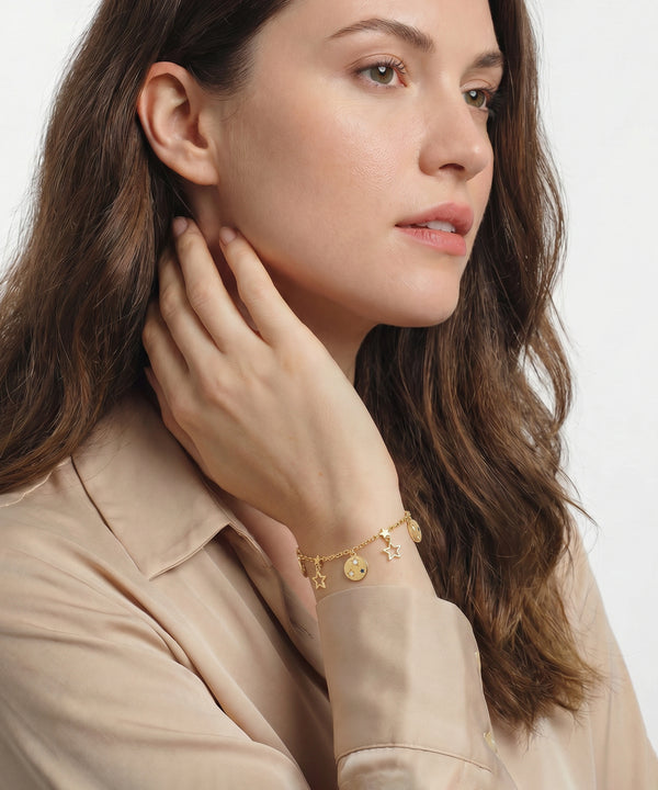 Woman wearing a gold bracelet with small charms on a plain background