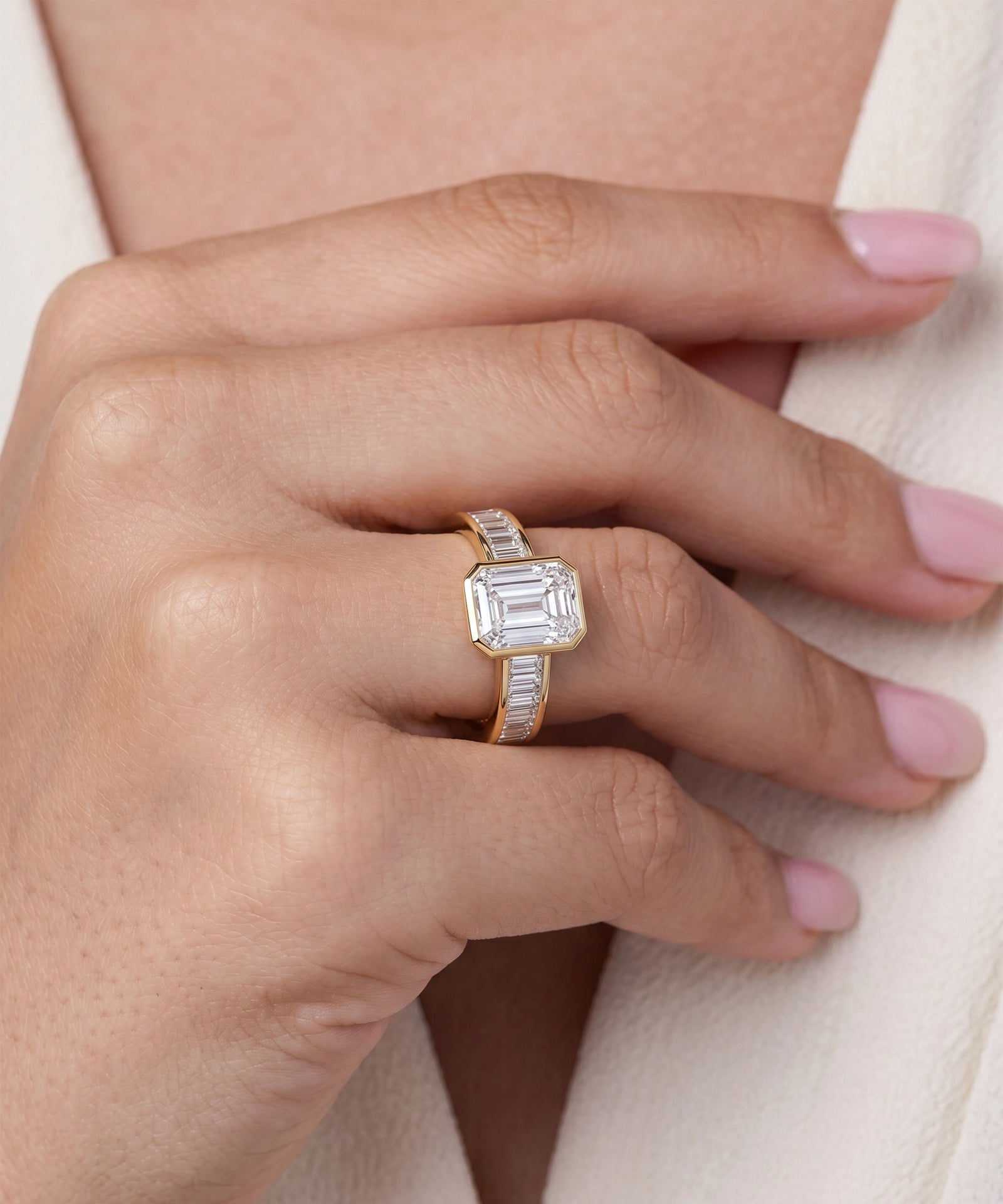 Gold ring with a diamond on a person's finger against a neutral background