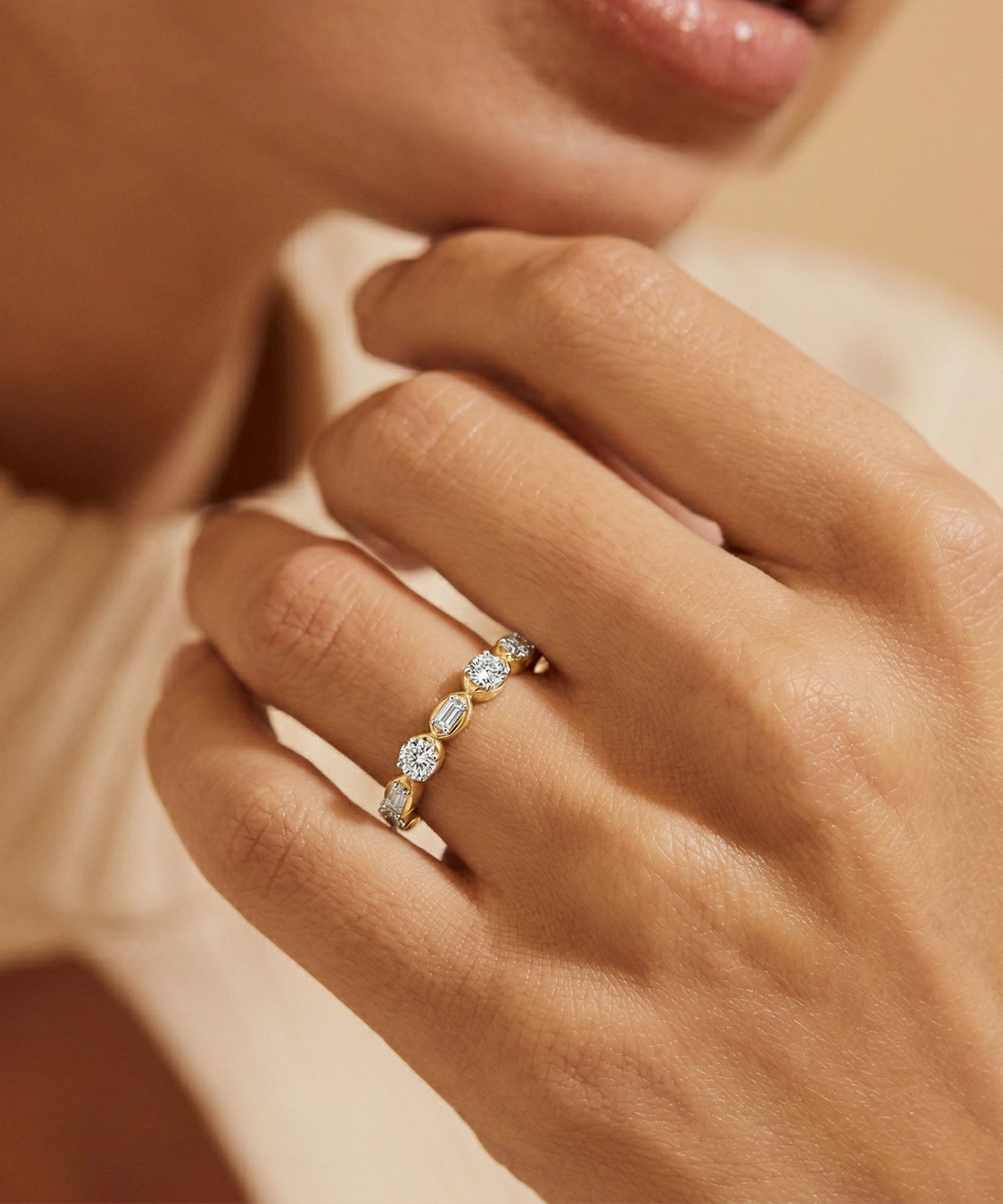 Close-up of a hand wearing a gold ring with diamonds on a neutral background
