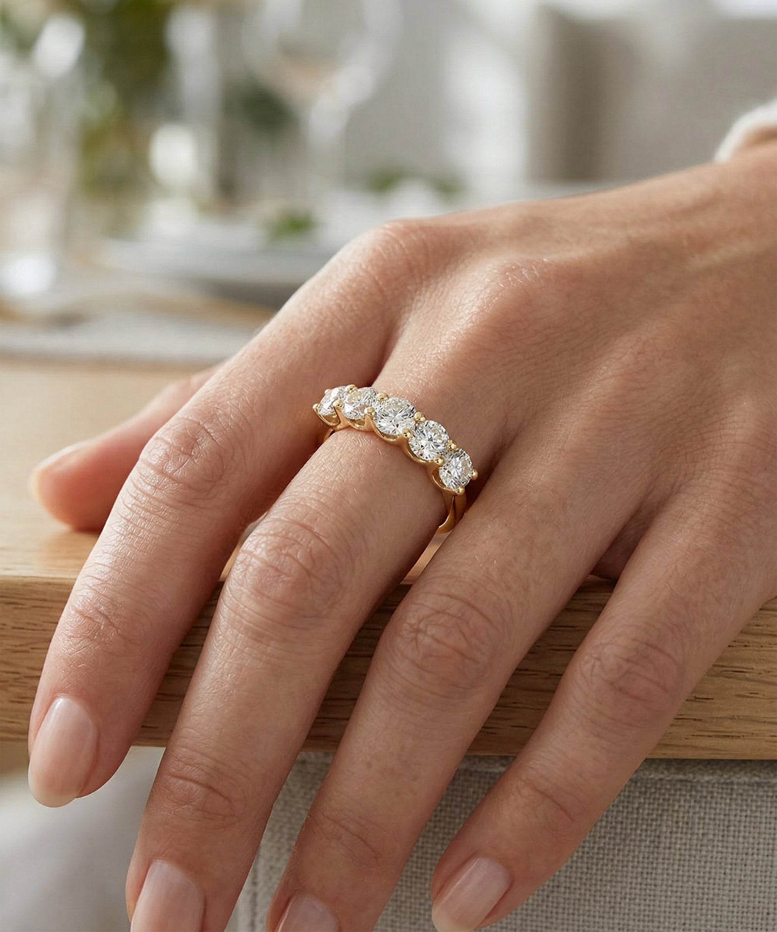 Hand wearing a gold ring with diamonds on a blurred indoor background