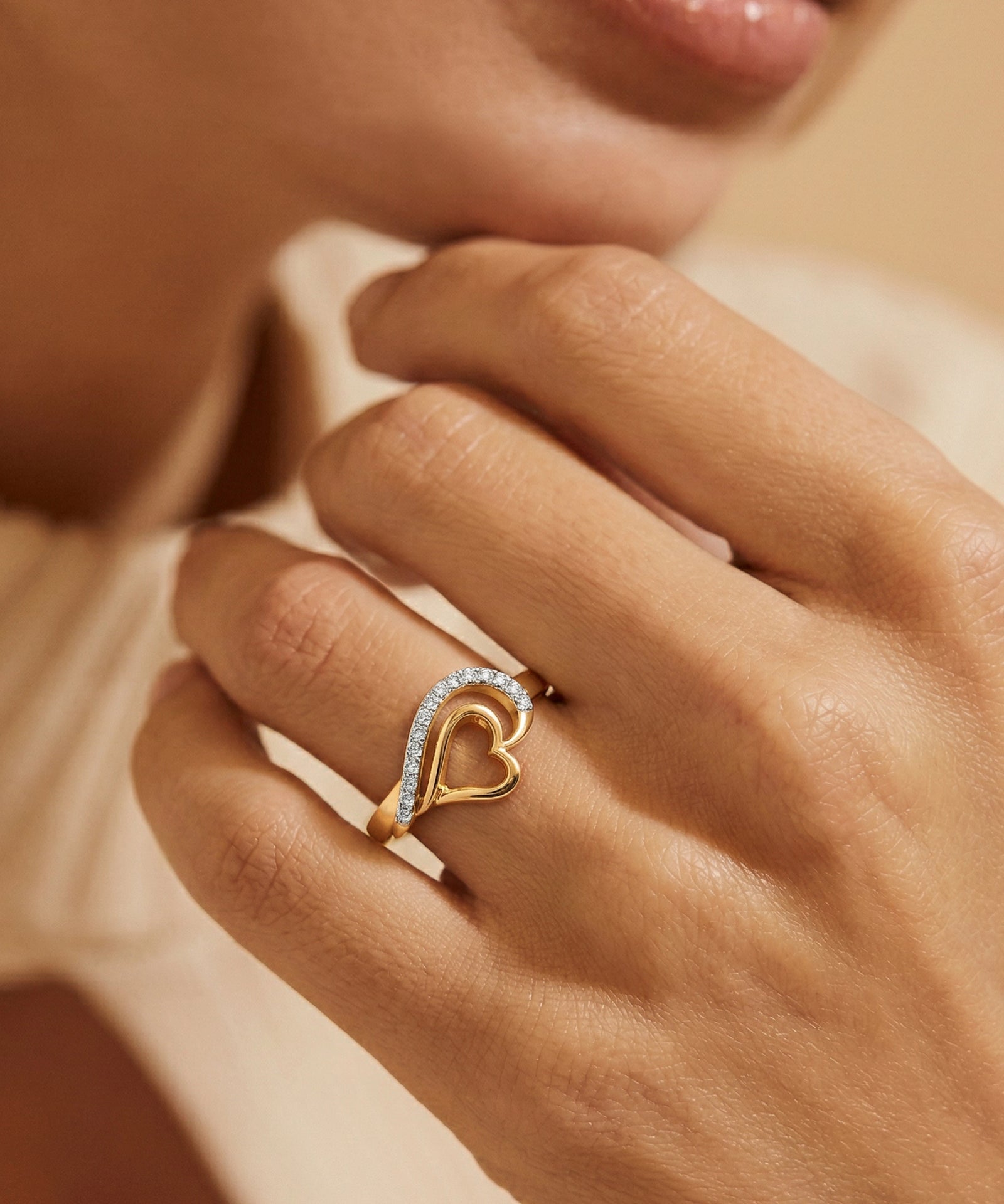 Heart-shaped ring with diamonds on a hand against a neutral background