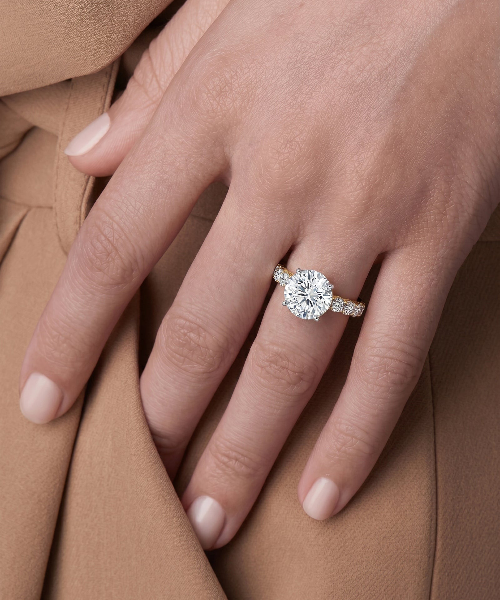 Close-up of a hand wearing a diamond ring on a brown fabric background