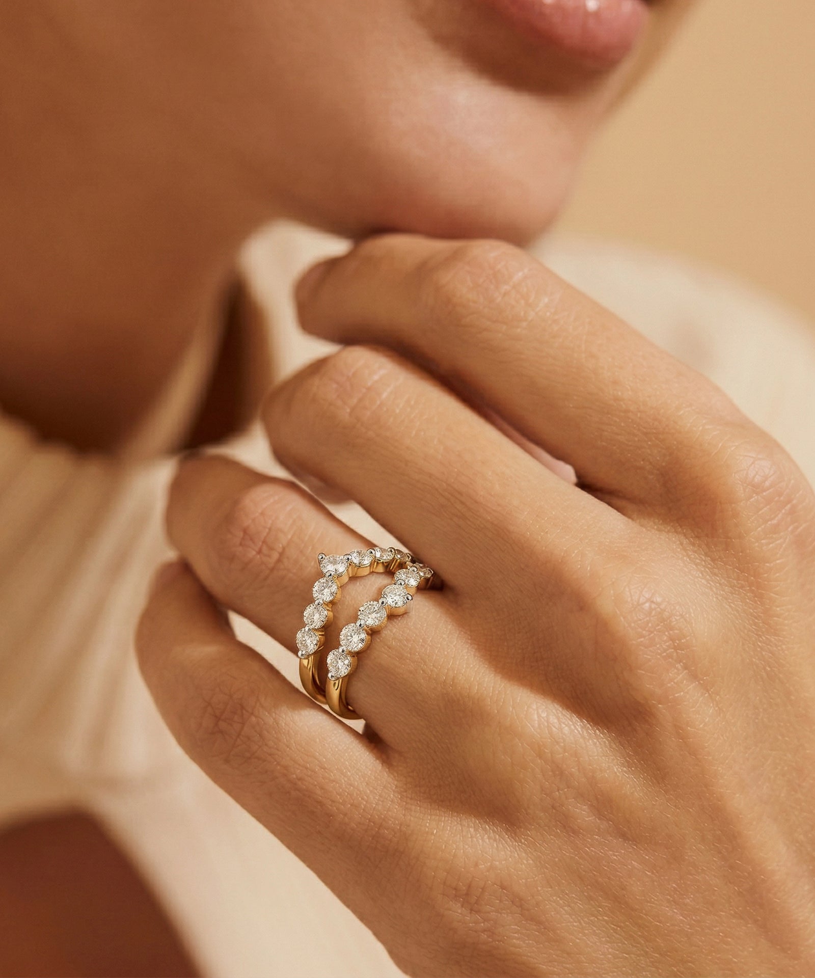 Close-up of a hand wearing a gold ring with diamonds on a neutral background