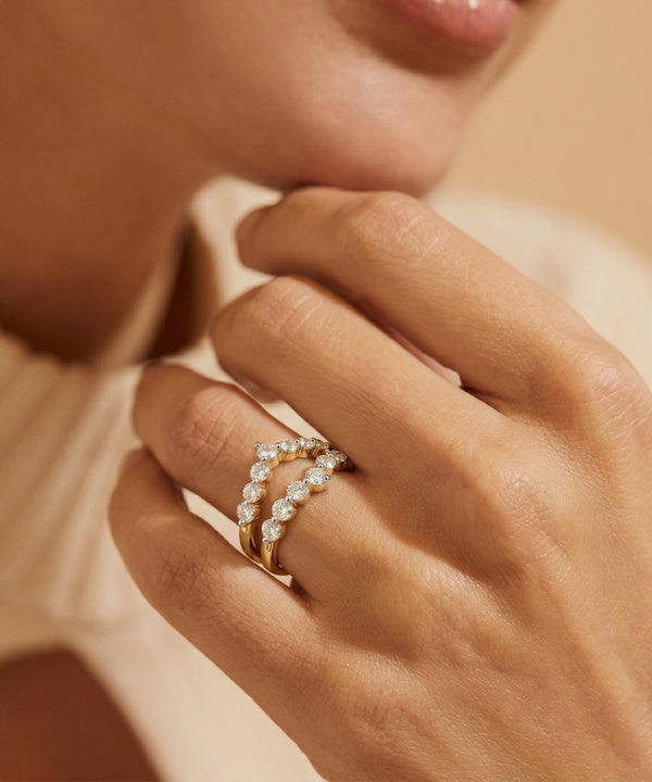 Close-up of a hand wearing a gold ring with diamonds on a neutral background