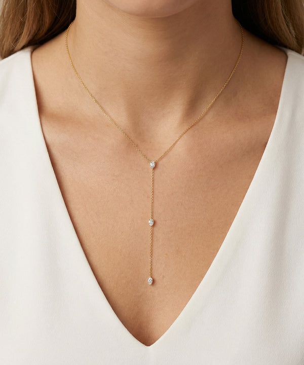 Gold necklace with small pendants on a person wearing a white top