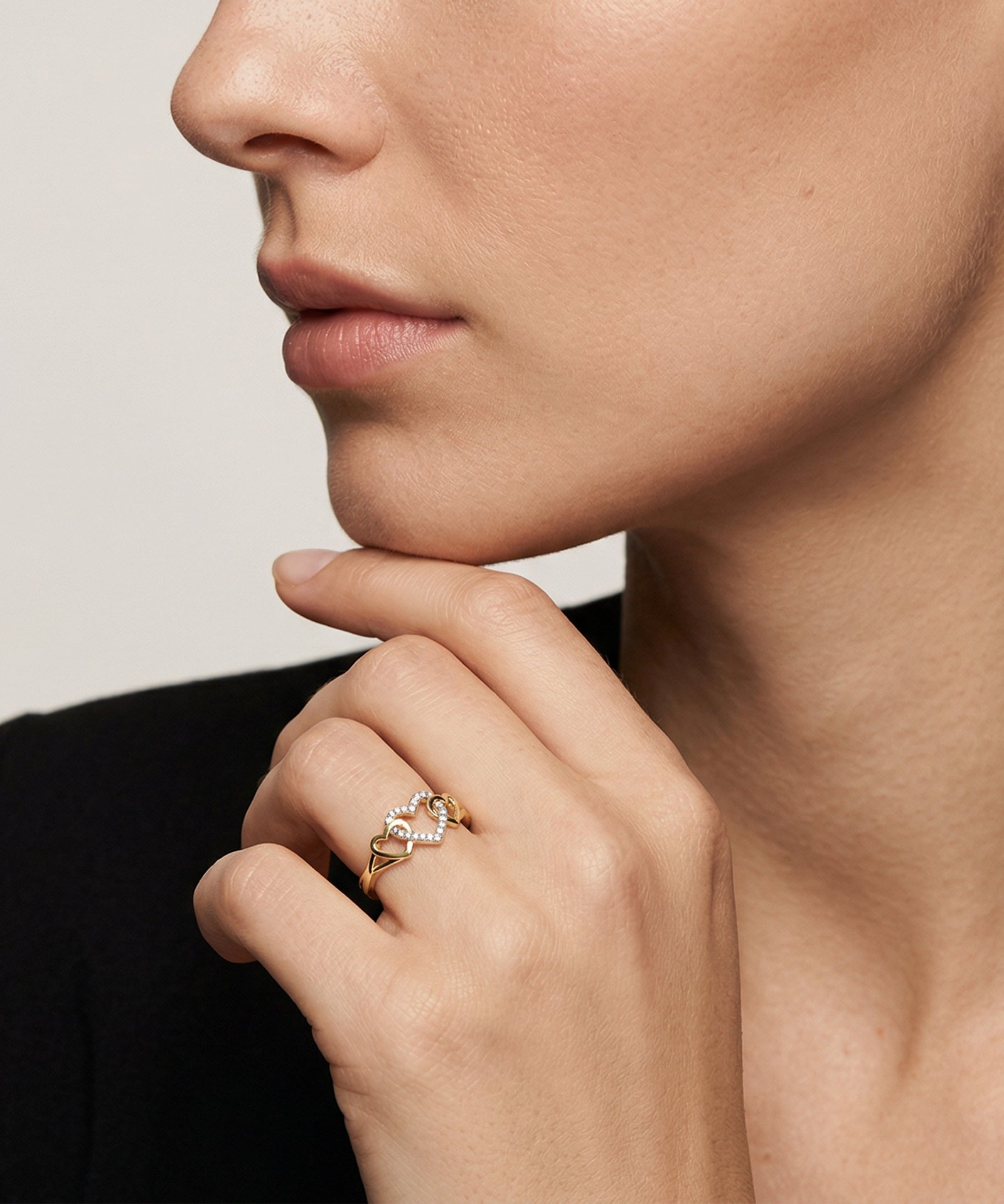 Close-up of a hand wearing a gold ring with a diamond on a neutral background