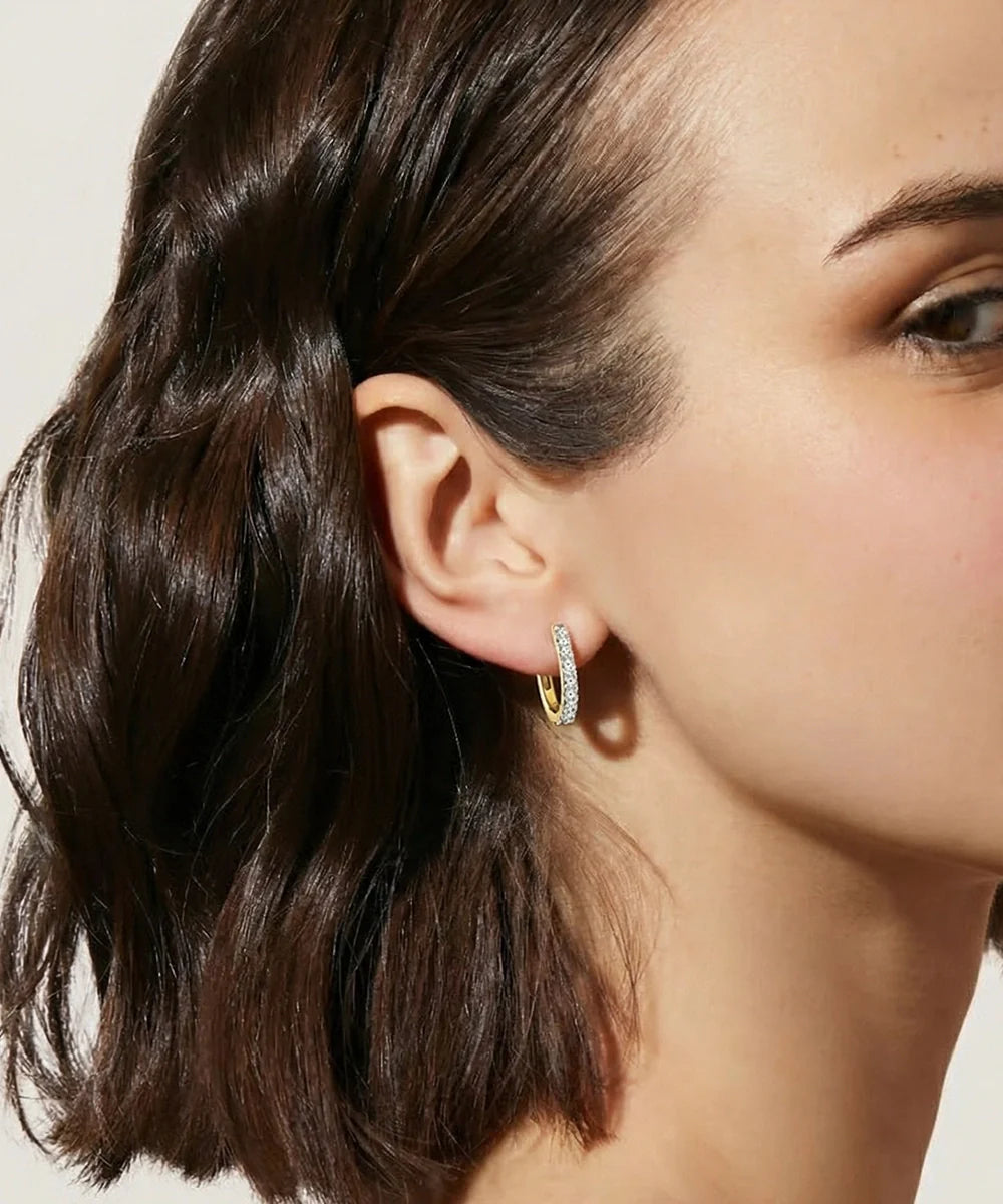 Close-up of a woman wearing gold hoop earrings with a neutral background