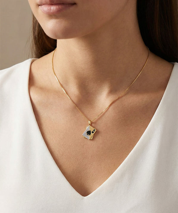 Gold necklace with a pendant worn by a person in a white top against a neutral background